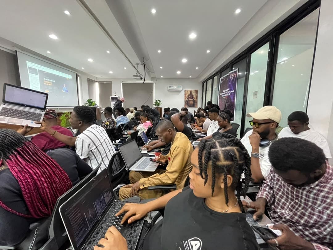 A woman working on a laptop in the foreground, with a full room of attendees and a presentation on screen behind her, at Antitect's first workshop in Lagos.