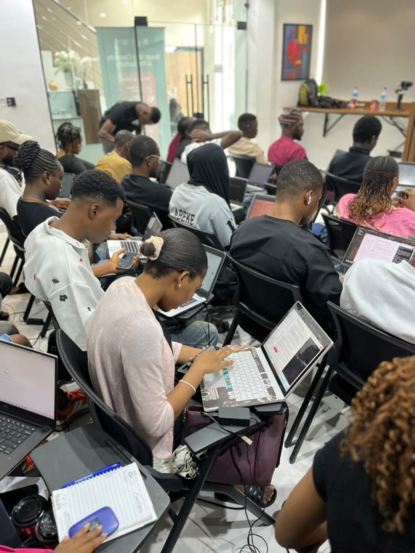 Over-the-shoulder view of someone working on a laptop while an instructor helps a participant nearby, at Antitect's first workshop in Lagos.